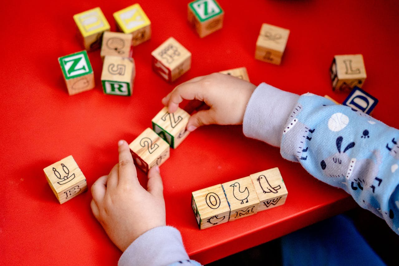 Young child engaging with wooden alphabet blocks on a vibrant red table, learning and playing.